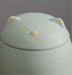 Mint cat-shaped memory urn with yellow accents on a gray background